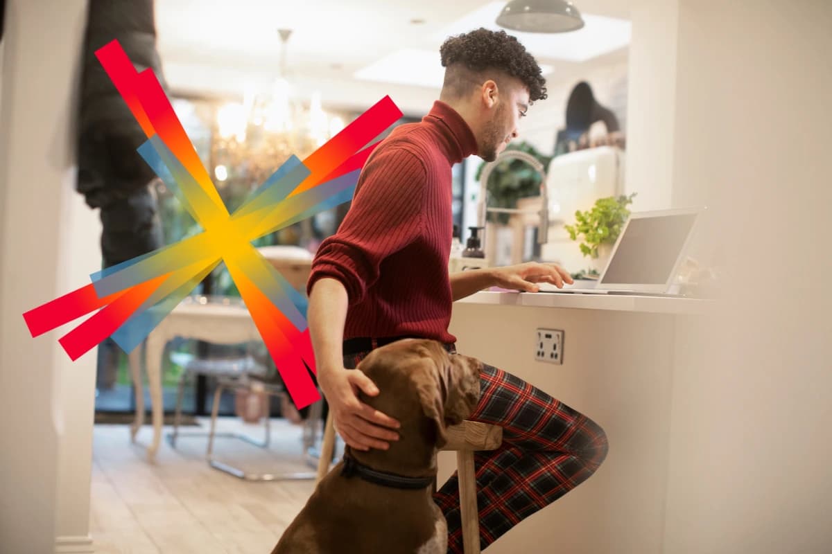  A man works on a laptop in a cozy kitchen while petting a dog sitting beside him.