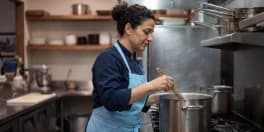 Woman cooking in large pot in industrial kitchen