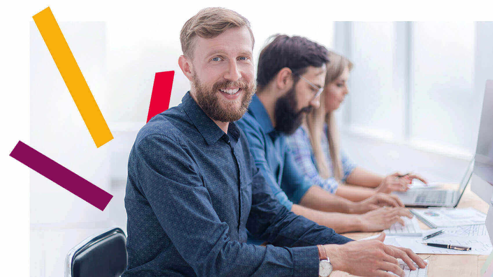 Group of workers at desk, one is smiling while on computer 